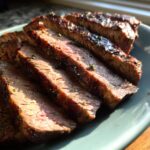 Close-up of perfectly cooked Alton Brown London broil, sliced and seasoned with herbs.