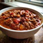 Close-up of a white bowl filled with hearty, homemade chili featuring ground beef, beans, and tomatoes.