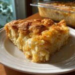 A slice of warm Apple Snickerdoodle Dump Cake on a white plate, with a golden brown topping.