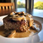 A close-up of a juicy baked hamburger steak topped with creamy mushroom sauce and sliced mushrooms.