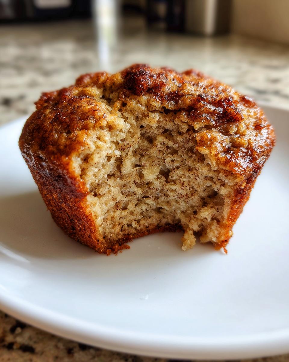 A close-up of a single banana protein muffin with a bite taken out, showing its moist interior.