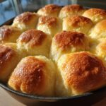 Close-up of golden-brown baked beef and bowtie pasta rolls in a cast iron skillet.