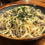 A close-up of a bowl of Beef and Garlic Butter Linguine, topped with fresh parsley and grated cheese.