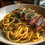A close-up of beef garlic butter linguine topped with perfectly sliced, medium-rare steak and fresh parsley.