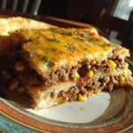 A close-up of a slice of beef taco casserole, featuring layers of seasoned ground beef, corn, and melted cheese.