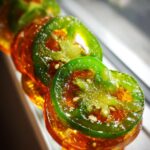 A close-up, shallow depth of field shot of glistening candied jalapenos, showcasing their vibrant green and amber hues.