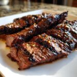 Close-up of perfectly grilled carne asada slices, glistening with a flavorful marinade and herbs.