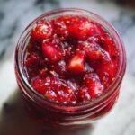 Close-up overhead view of a jar filled with glistening homemade Christmas jam, showcasing chunks of strawberries and seeds.