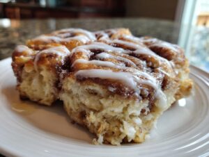 Close-up of a fluffy slice of cinnamon roll casserole drizzled with white icing.