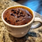 A warm Cottage Cheese Microwave Brownie topped with chocolate chips in a white mug.