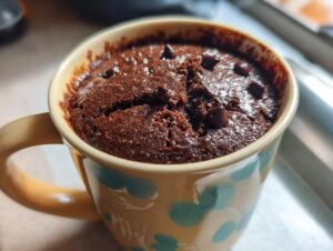 A close-up of a rich chocolate Cottage Cheese Microwave Brownie baked in a decorative mug, topped with chocolate chips.