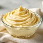 A close-up of a glass bowl filled with smooth, creamy garlic aioli, swirled on top.