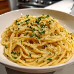 A close-up of a bowl of creamy lemon pasta, topped with fresh parsley and grated cheese.