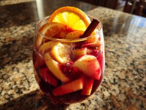 A glass of fall sangria filled with red wine, apples, oranges, lemons, and a cinnamon stick.