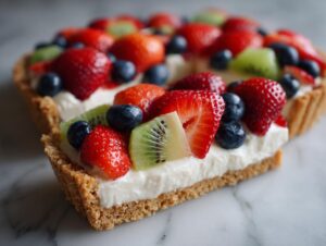 A slice of fruit pizza sugar cookie topped with cream cheese frosting and fresh strawberries, blueberries, and kiwi.