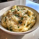 A close-up of fluffy garlic parmesan mashed potatoes in a white bowl, topped with grated parmesan and fresh parsley.