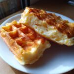 Close-up of two golden-brown high protein waffles on a white plate, showing their fluffy interior.