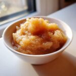 A close-up of a white bowl filled with chunky, warm homemade applesauce, sprinkled with cinnamon.