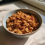 A light blue bowl filled with golden brown homemade granola, featuring oats, nuts, and dried fruit.