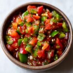 Close-up of a rustic bowl filled with vibrant homemade salsa, featuring chopped tomatoes, green peppers, and cilantro.