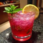 A close-up of a glass filled with honey lemon pink soda, ice, mint, and a lemon slice.