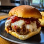 Close-up of a juicy Italian sub slider with a meatball, melted mozzarella cheese, and marinara sauce on a bun.
