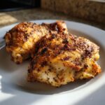 Close-up of two perfectly cooked lemon pepper chicken thighs on a white plate, seasoned with spices.