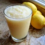 A tall glass of creamy lemonade, with whole lemons in the background, perfect for a fall harvest salad.