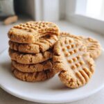 A stack of classic peanut butter cookies with fork marks, one cookie bitten into.