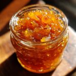 Close-up of a glass jar filled with glistening, amber-colored Pear Preserves, showing chunks of pear and seeds.
