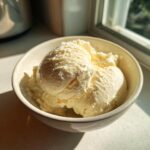 Close-up of three scoops of creamy protein ice cream in a light-colored bowl, bathed in sunlight.