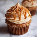 Close-up of a perfectly frosted pumpkin spice cupcake topped with caramel drizzle and cinnamon.