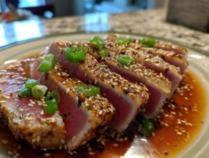 Close-up of perfectly seared ahi tuna slices coated in sesame seeds and green onions, served in a savory sauce.