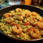 Close-up of shrimp orzo in lemon garlic sauce, garnished with parsley, served in a black skillet.
