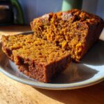 Close-up of two moist slices of sourdough pumpkin bread on a plate, showcasing its rich orange color and texture.