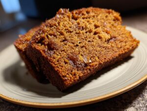 Close-up of two moist slices of sourdough pumpkin bread on a plate, showcasing its rich texture and warm color.