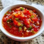 A white bowl filled with vibrant, chunky tomato salsa, featuring diced tomatoes, green peppers, and onions.