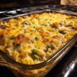 Close-up of a bubbling Tuna Casserole with golden cheese topping and visible peas in a glass baking dish.