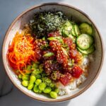 A vibrant Tuna Poke Bowl filled with marinated tuna, rice, edamame, shredded carrots, cucumber slices, and nori.
