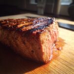 Close-up of a perfectly cooked tuna steak, glistening with marinade, resting on a wooden cutting board.