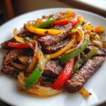 Close-up of perfectly cooked steak fajitas featuring sliced steak, sautéed onions, and colorful bell peppers.