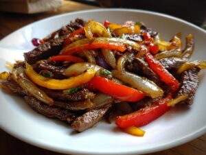 Close-up of savory steak fajitas featuring strips of seasoned beef mixed with sautéed red, yellow, and white onions and peppers.