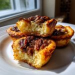 Three golden-brown pecan tassies stacked on a white plate, one of which is bitten into, showing the soft interior.