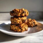 Three oatmeal breakfast cookie stacked on a white plate, featuring visible oats and chocolate chips.