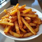 Close-up of golden brown air fryer french fries heavily seasoned with salt and spices in a white bowl.