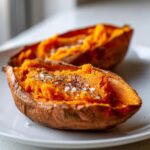 Two halves of fluffy baked sweet potatoes, seasoned with coarse salt and pepper, ready to eat.