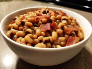 A white bowl filled with savory black eyed peas cooked in broth and topped with crispy bacon pieces.