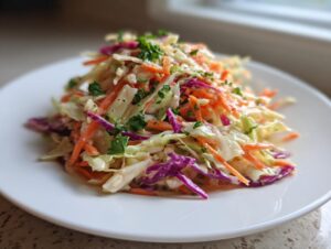 A vibrant mound of creamy cabbage salad featuring shredded green cabbage, red cabbage, and carrots, garnished with parsley.