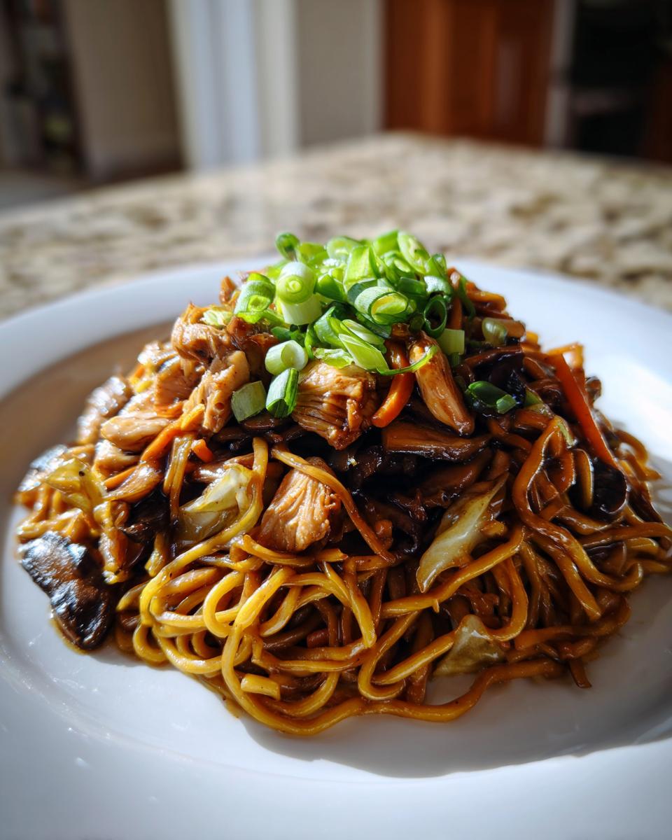 A mound of savory chicken chow mein recipe noodles, chicken, and vegetables topped with fresh green onions.