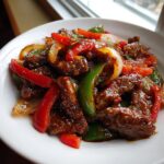 Close-up of glossy, saucy pepper steak mixed with vibrant red and green bell peppers and onions.